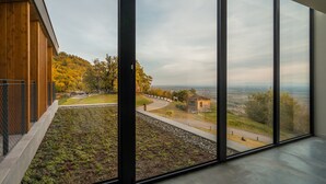 En moderne bygning med store vinduer, der giver udsigt over et anlagt område med en sti og en mindre bygning.