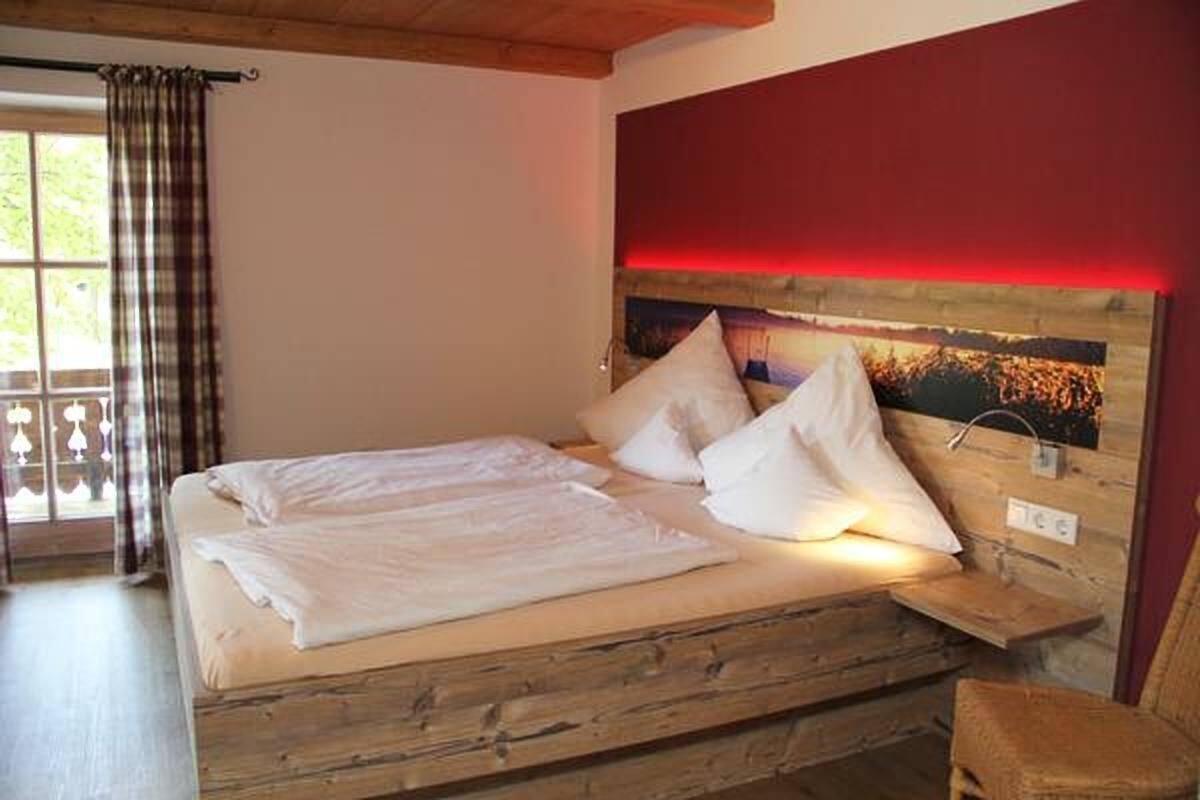 A bed with white linens, a wooden headboard, and a nightstand with a lamp.