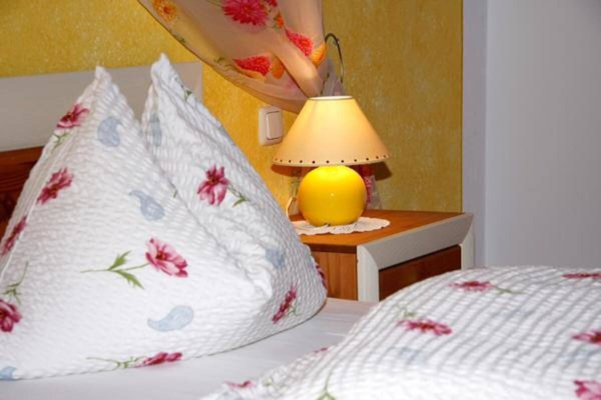 A bed with floral bedding, a bedside lamp, and a small table with a yellow object on it.