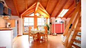 A spacious kitchen with wooden beams, a dining area with a table and chairs, and a staircase. - Wachinger Hof (Bad Feilnbach)