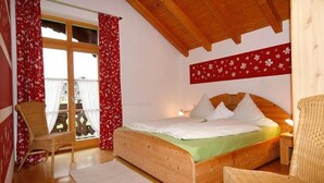 A wooden bed with a green bedspread in a room with red floral curtains and a wooden ceiling. - Wachinger Hof (Bad Feilnbach)