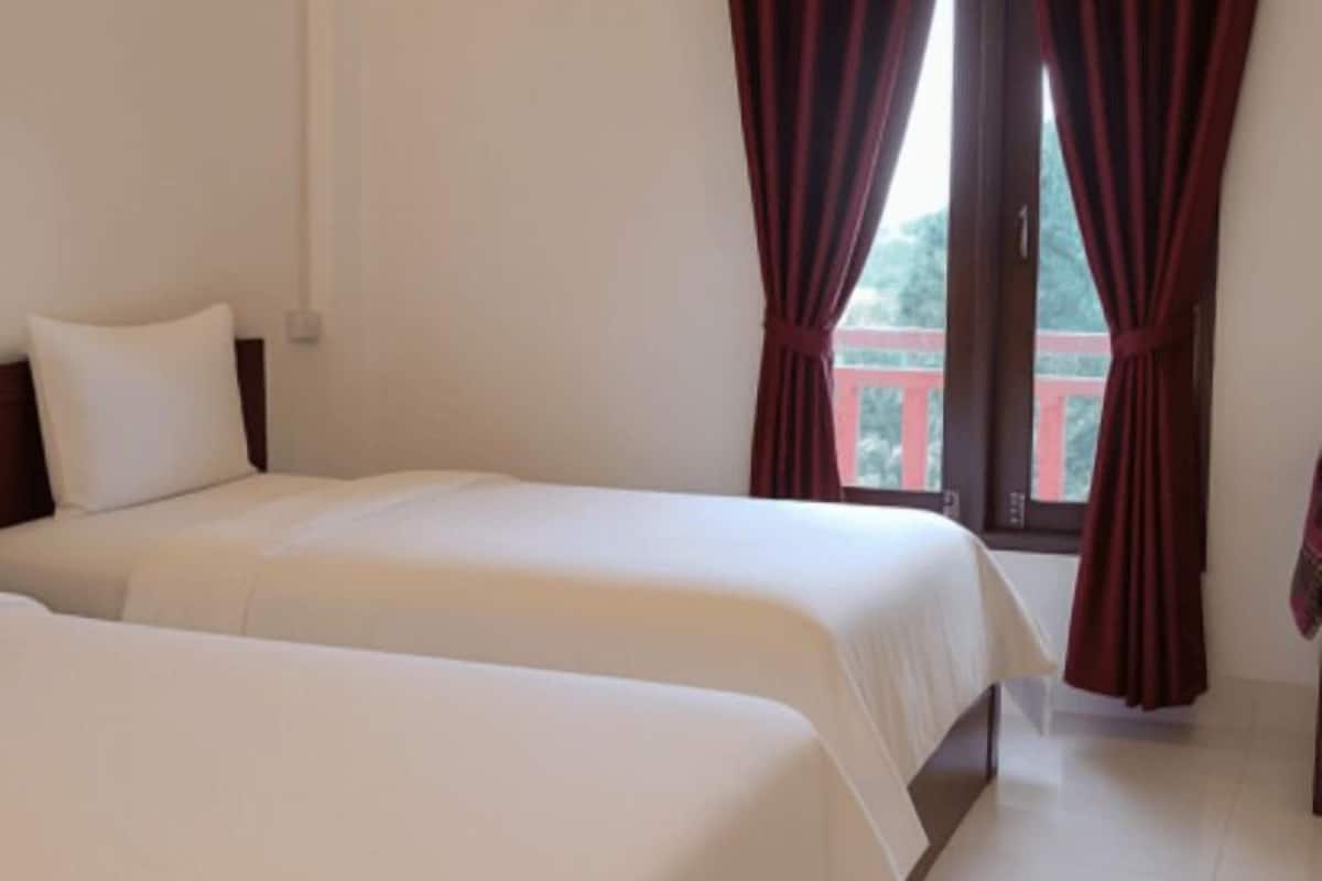 A hotel room with two beds, a window with curtains, and a view of a red balcony.