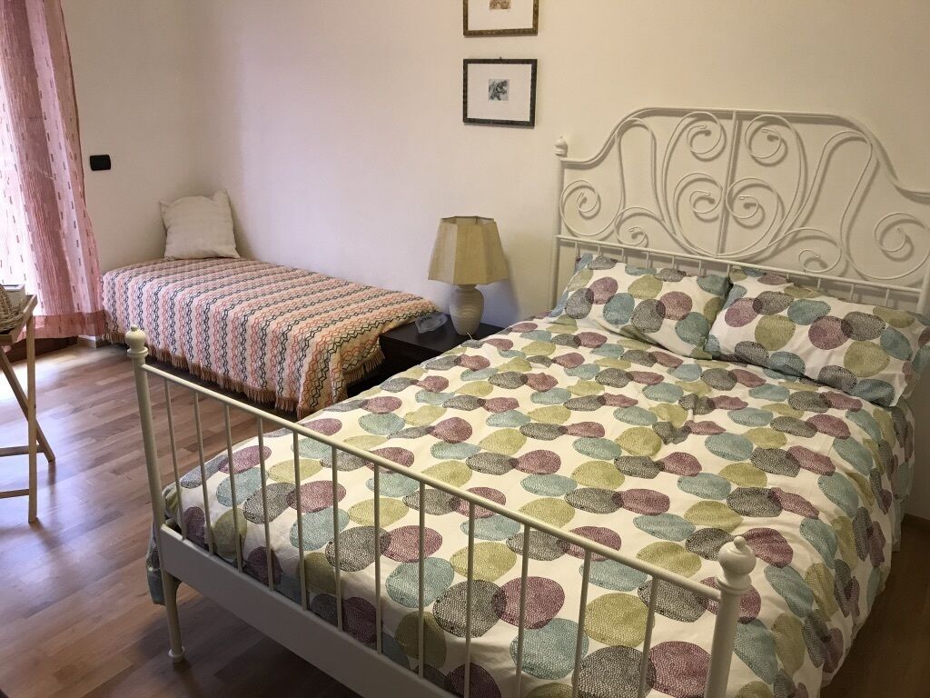 Un dormitorio con dos camas, piso de madera, cabecera de metal y una lámpara en una mesita de noche.