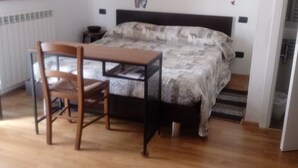 Ein Schlafzimmer mit einem Bett, einem Holzstuhl, einem kleinen Tisch, einem Heizkörper und einem Bild an der Wand.