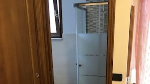 Ein Korridor, der zu einem durch Glas geschlossenen Raum mit einem Holztürrahmen und einem kleinen Tisch mit einer Lampe führt.