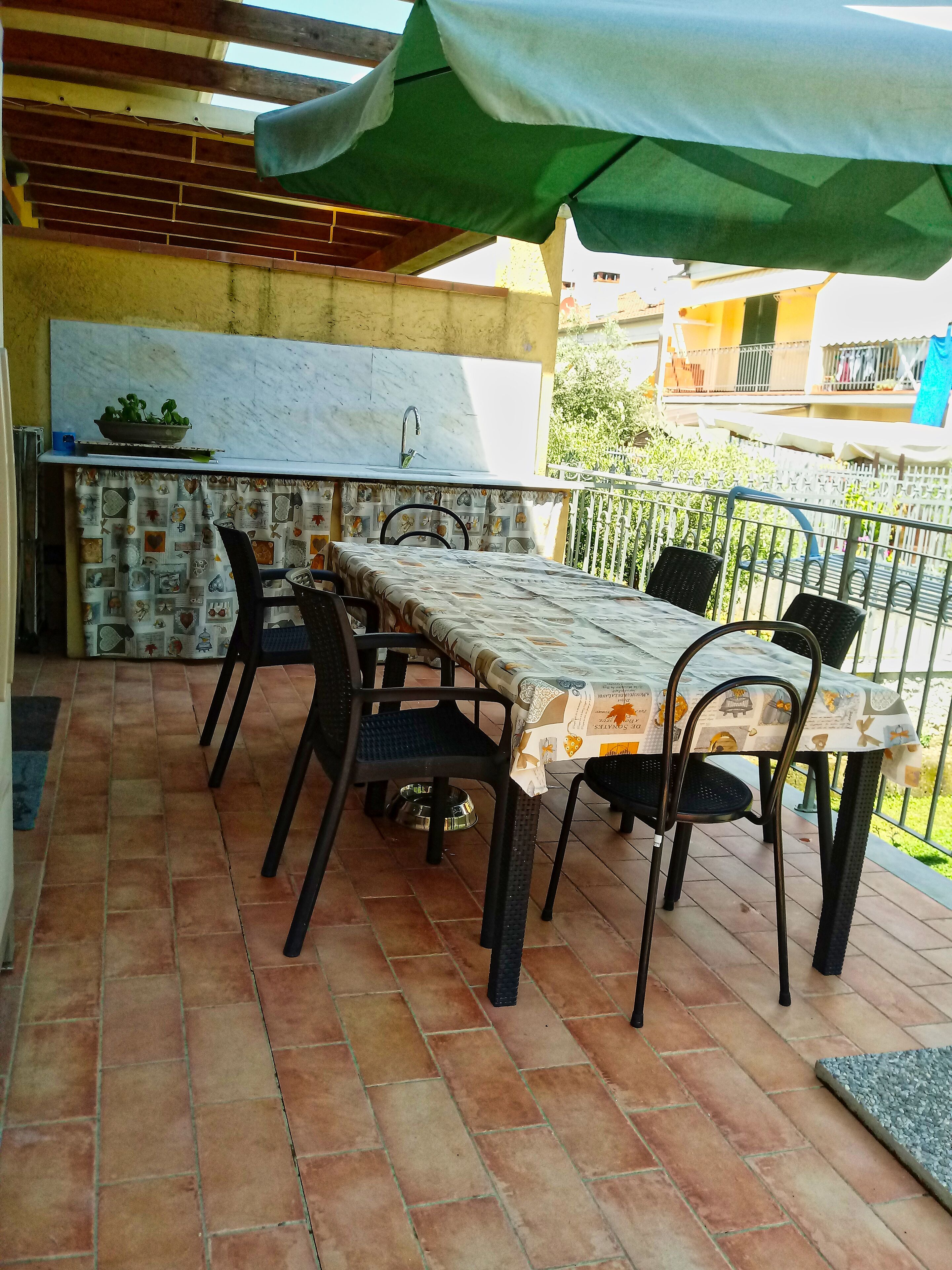 An outdoor patio with a table and chairs, a grill, and a covered area with a green umbrella.