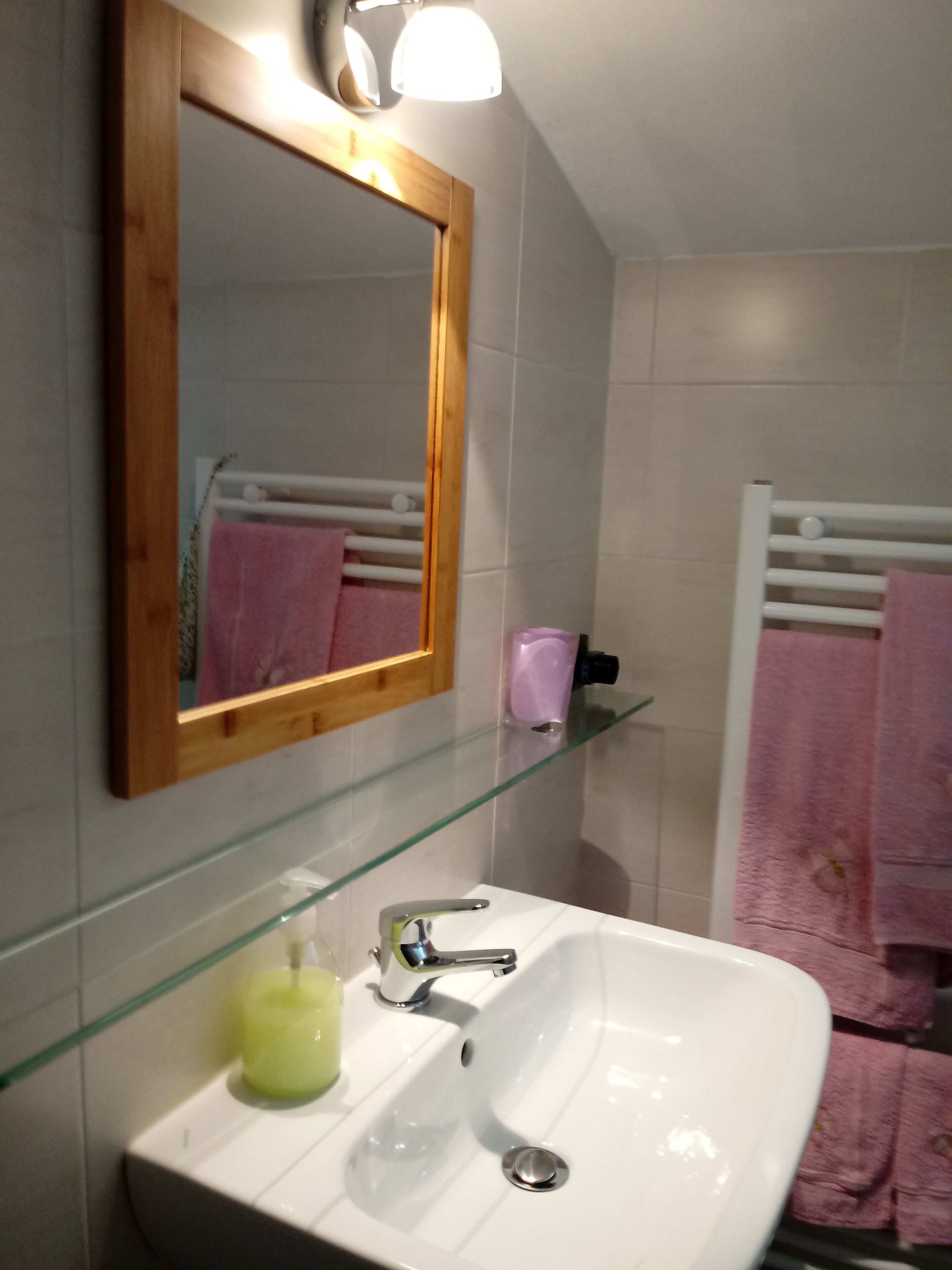 Ein Badezimmer mit einem weißen Waschbecken, einem Spiegel und einer Glasablage.