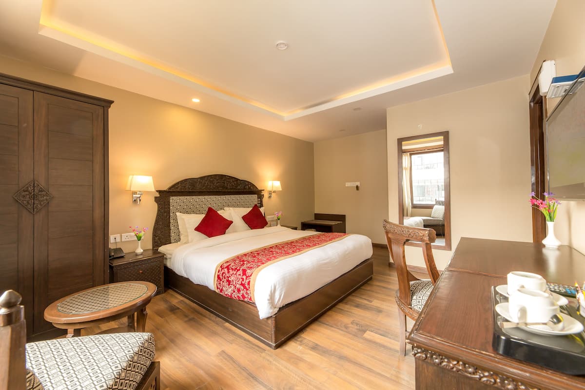 A hotel room with a large bed, wooden floor, a dining table with chairs, a small round table, and a mirror on the wall.