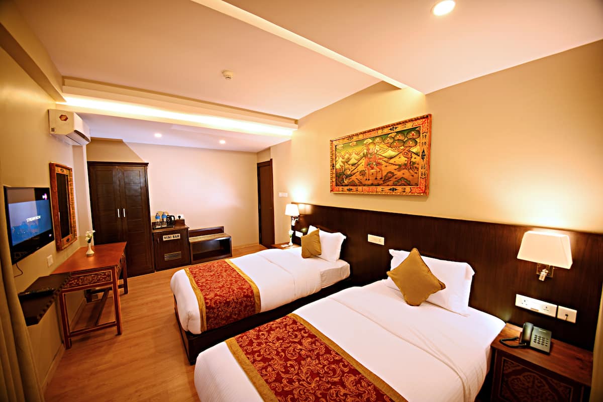 A hotel room with two beds, a desk, a TV, and a minibar.