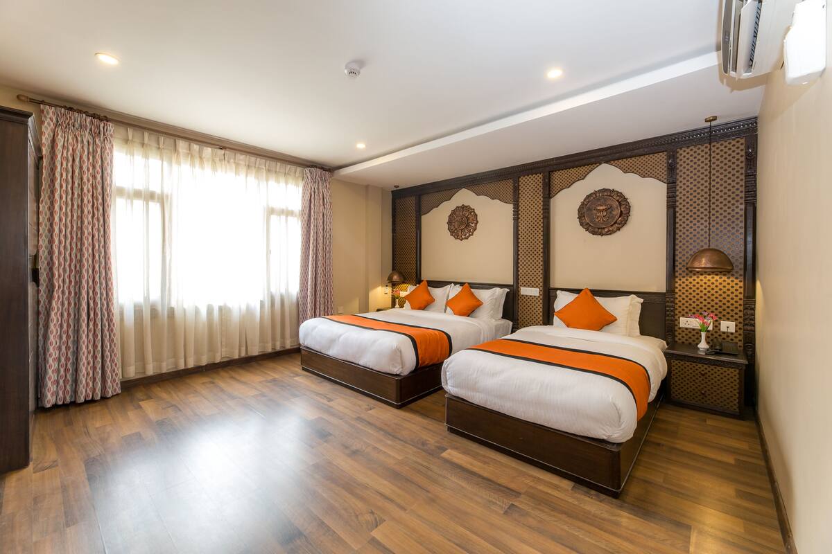 A hotel room with two beds, wooden flooring, a large window with curtains, and a decorative wall panel.