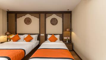 Hotelkamer met twee bedden, elk met witte beddengoed en oranje accenten. Er zijn decoratieve wandpanelen en een klein tafeltje met een lamp.