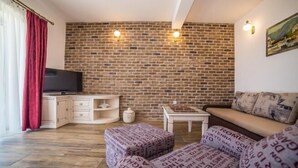 Ein Wohnzimmer mit Backsteinwand, Fernseher, einer Couch und einem kleinen Tisch.