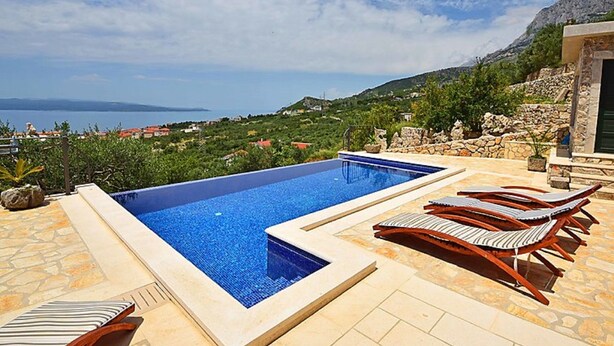 Ein rechteckiger Pool mit klar blauem Wasser, umgeben von Steinfliesen und Holzliegen.