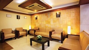 A spacious lounge area with sofas and armchairs arranged around a central coffee table, featuring a stone accent wall and recessed ceiling lighting. - Broad Bean Cochin (Kanayannur)