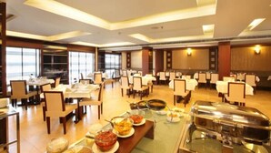 A spacious dining area with multiple tables and chairs, buffet setup with various food items, and large windows providing natural light. - Broad Bean Cochin (Kanayannur)