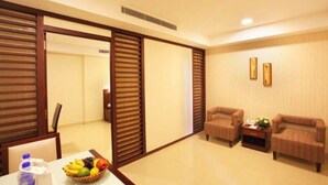 A hotel room with a sliding door, a dining table with fruit, two sofas, and a small table with a vase. - Broad Bean Cochin (Kanayannur)