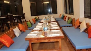 Un restaurant avec de longues tables dressées pour le repas, des sièges rembourrés de couleur bleue et une variété de coussins aux couleurs vives.