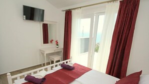A hotel room with a bed, a white dresser, a mirror, a TV, and a view of the sea. - Villa Belvedere (Makarska)