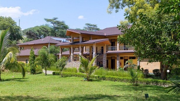 A two-story building with a covered outdoor area, surrounded by greenery and trees.