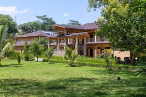 Un edificio de dos pisos con un espacio exterior techado, rodeado de vegetación y árboles.