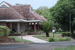 Un edificio de piedra con techo de tejas, un sendero de piedra que lleva a la entrada y un jardín bien cuidado con una palmera y arbustos.
