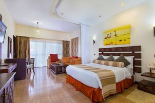 Habitación de hotel con cama, escritorio, silla, televisor y un cuadro en la pared.