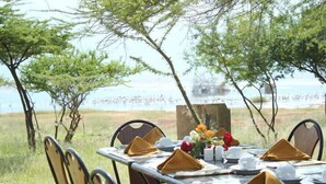 An outdoor dining table set with chairs, a painting, and a vase of flowers.