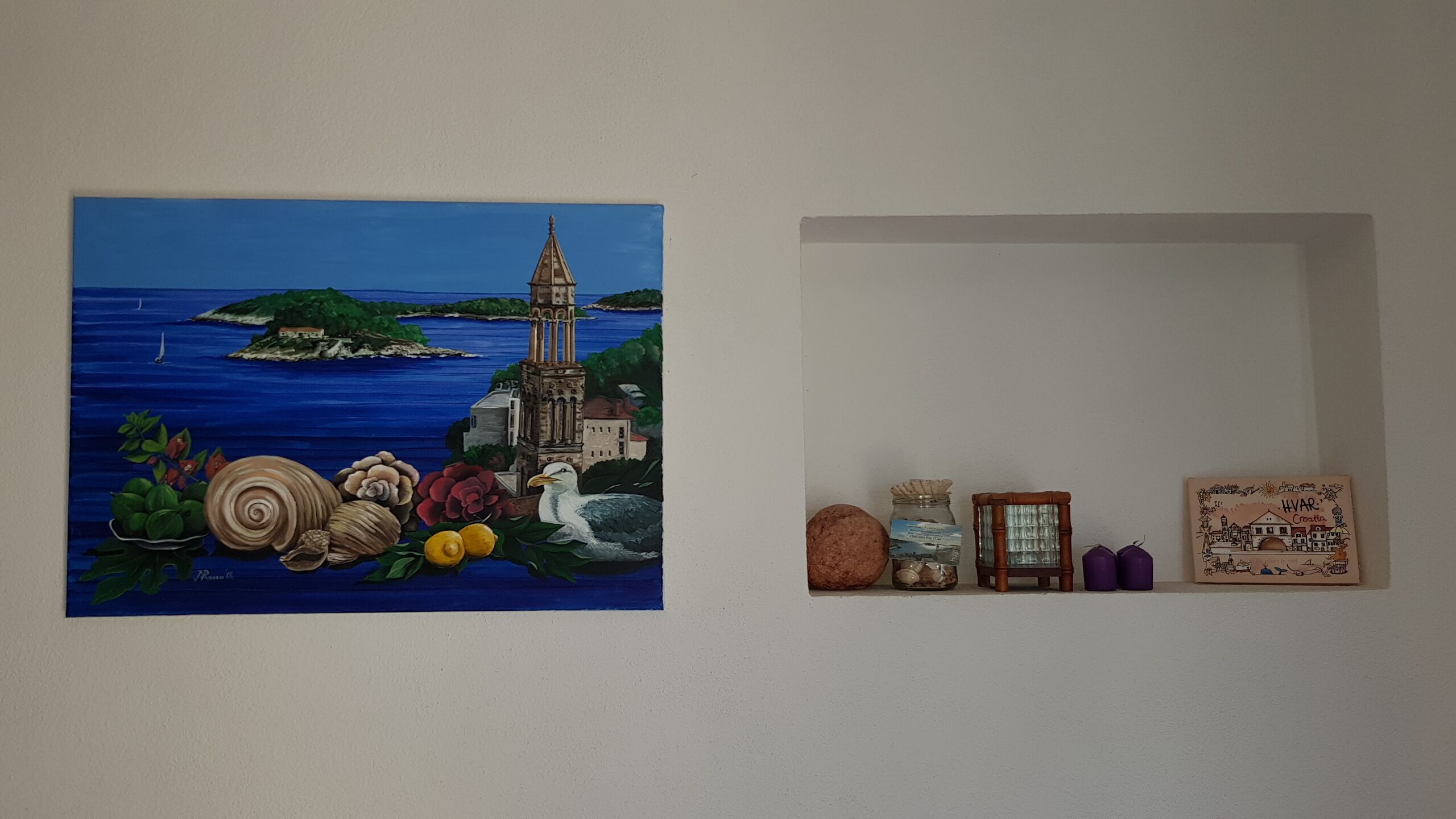 A wall with a painting of a coastal scene and a small shelf with decorative items.