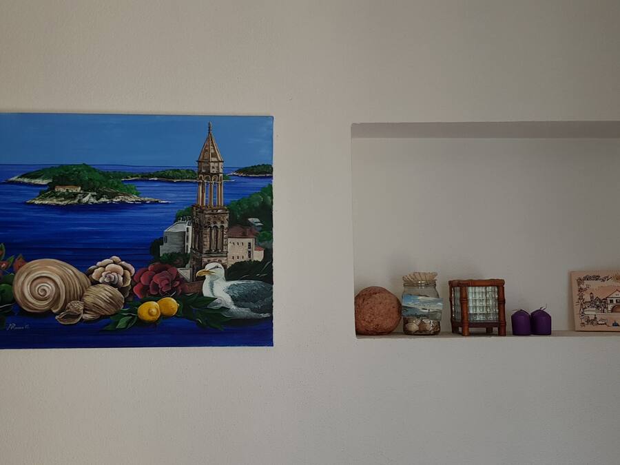 A wall with a painting of a coastal scene and a small shelf with decorative items.
