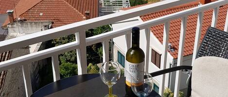 Un balcon avec une table, deux verres à vin et une bouteille de vin. La vue comprend un port de plaisance avec des bateaux et une église.