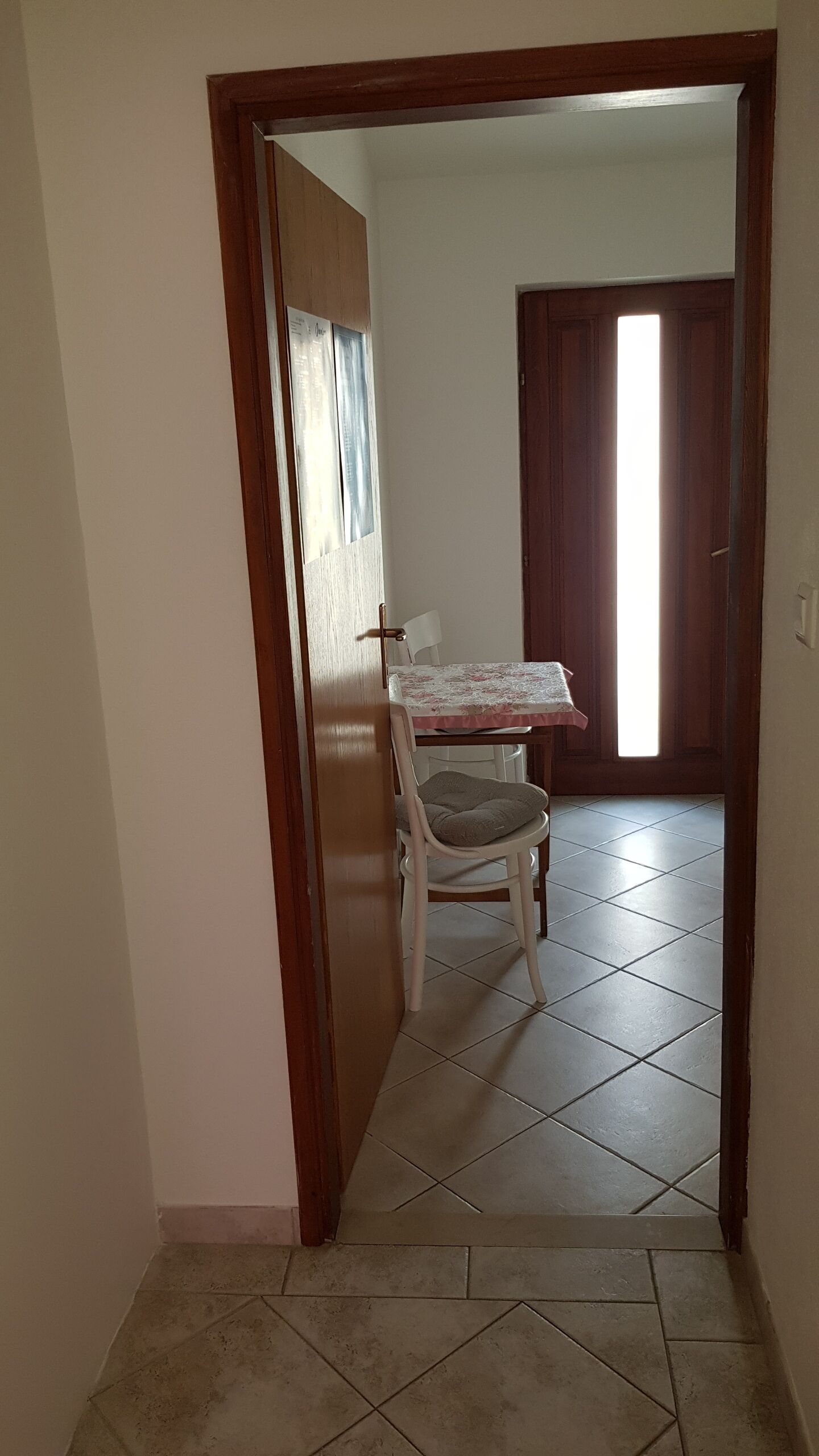 A hallway with a dining area featuring a table and two chairs, a tiled floor, and a wooden door.