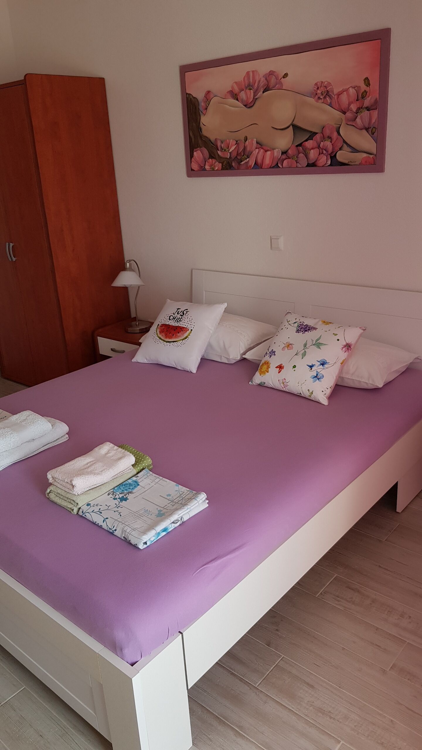 Un dormitorio con colcha morada, almohadas blancas y un cuadro de flores en la pared.