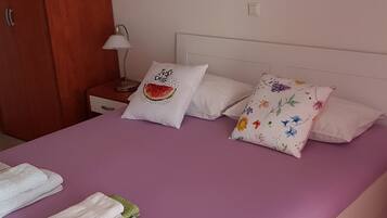 Un dormitorio con colcha morada, almohadas blancas y un cuadro de flores en la pared.