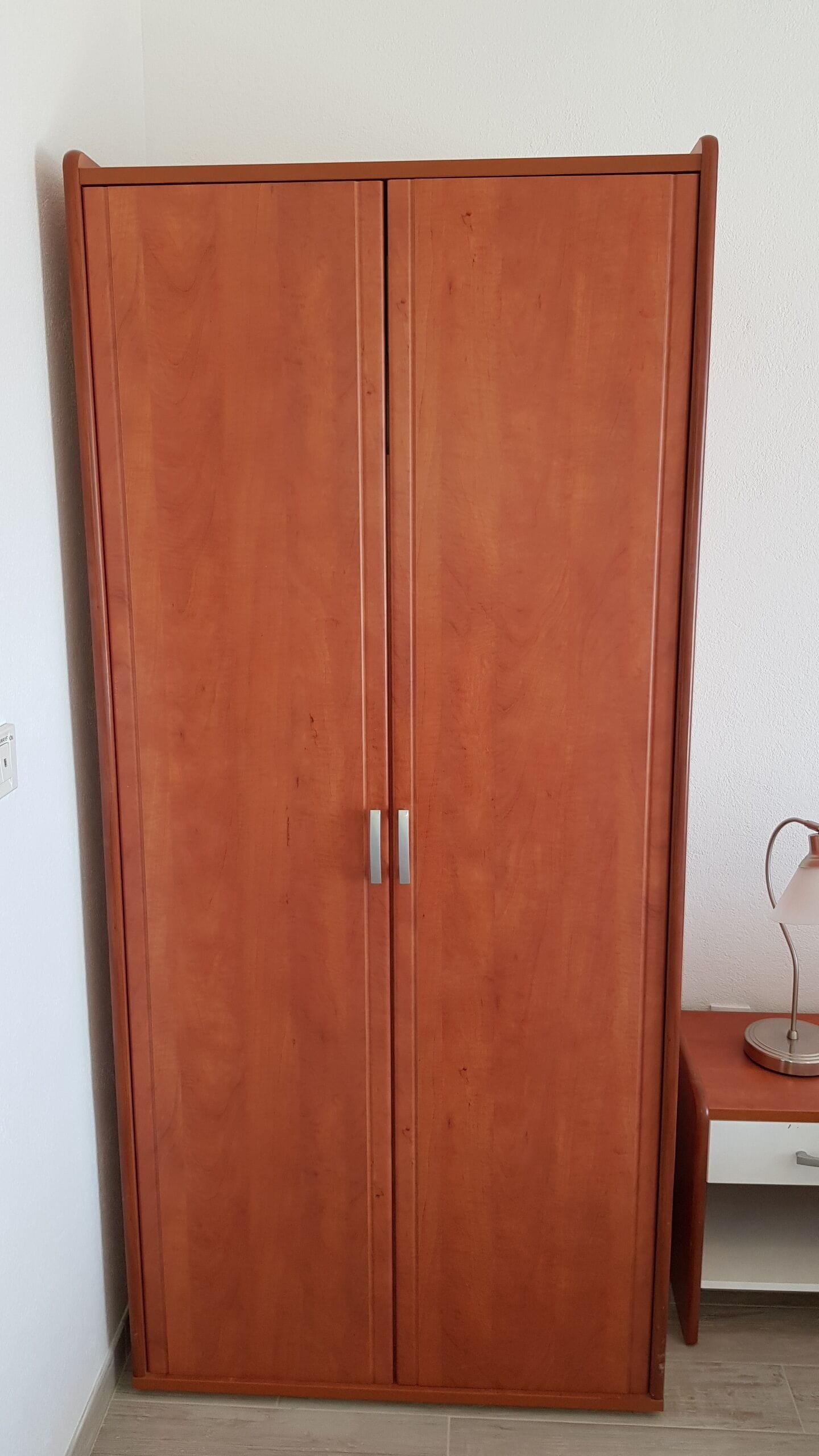Un armario de madera grande con dos puertas y un pequeño banco a un lado.