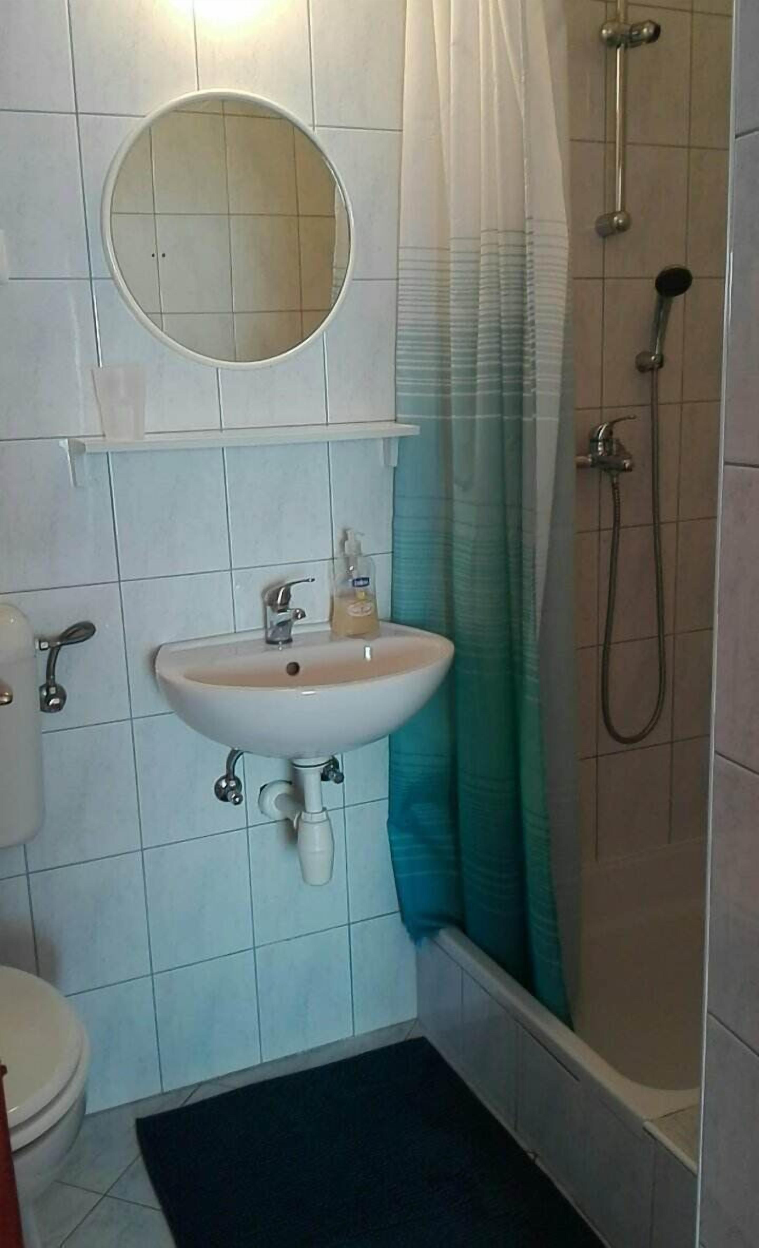 Une salle de bain avec un lavabo blanc, des toilettes, une douche et un miroir rond.