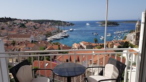 A balcony with a table and chairs overlooking a marina with boats and a coastal town. - Bocin Rosso Apartments (Hvar)