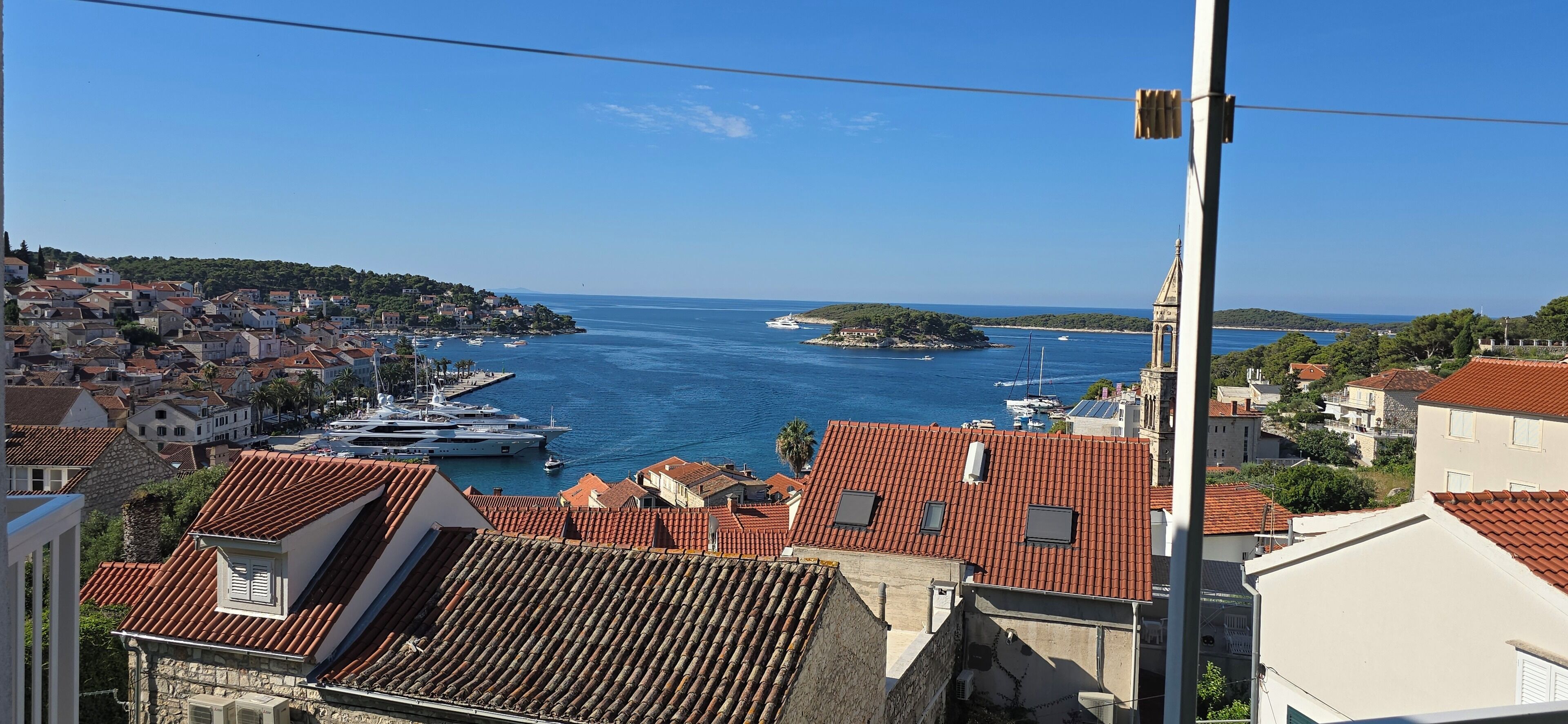 Une ville côtière aux bâtiments aux toits de tuiles rouges, un port de plaisance rempli de bateaux et une mer d’un bleu limpide.