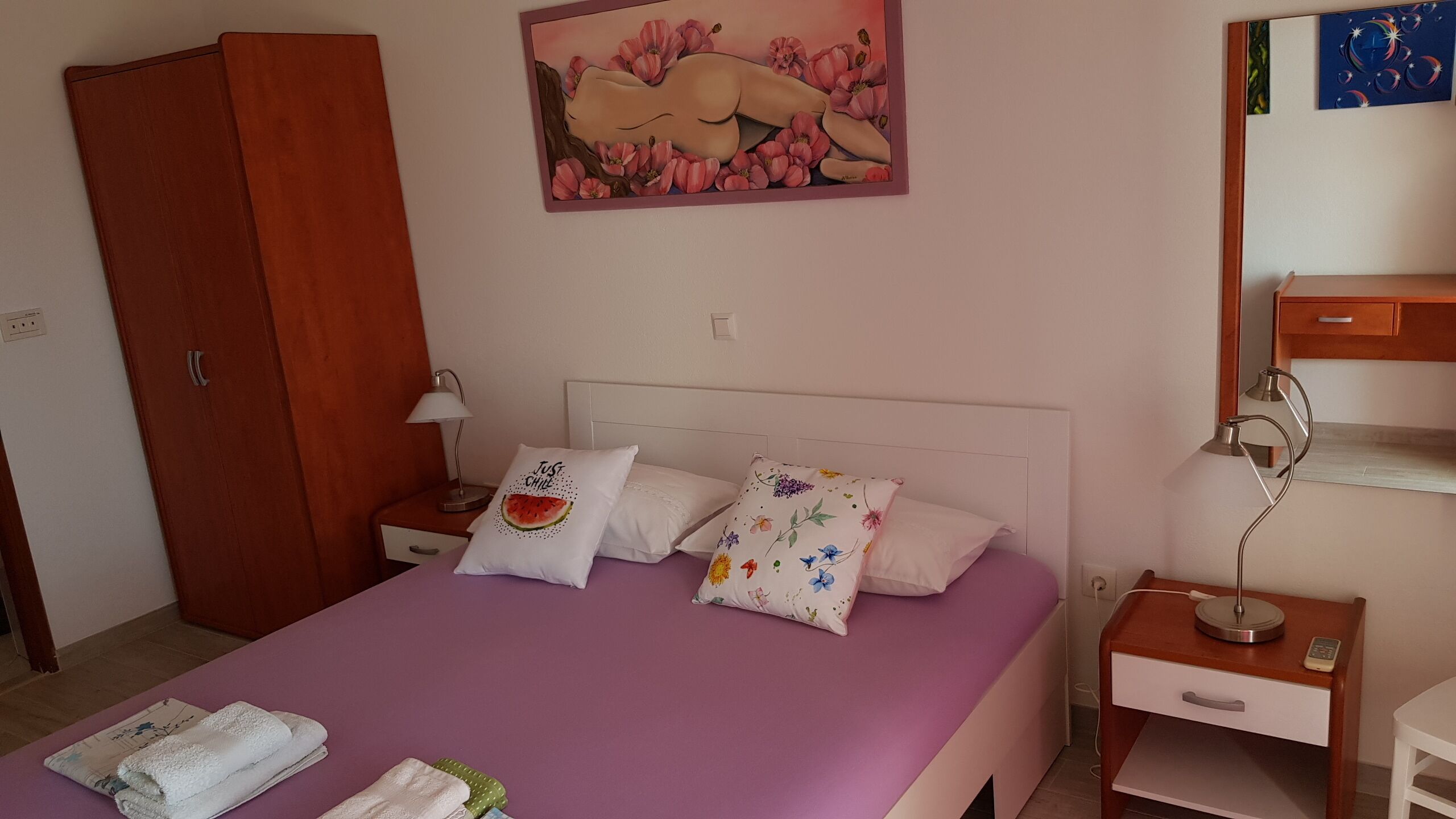 A bedroom with a bed, a nightstand, a lamp, a wardrobe, and a painting on the wall.