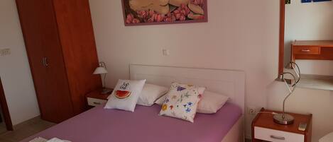 A bedroom with a bed, a nightstand, a lamp, a wardrobe, and a painting on the wall.