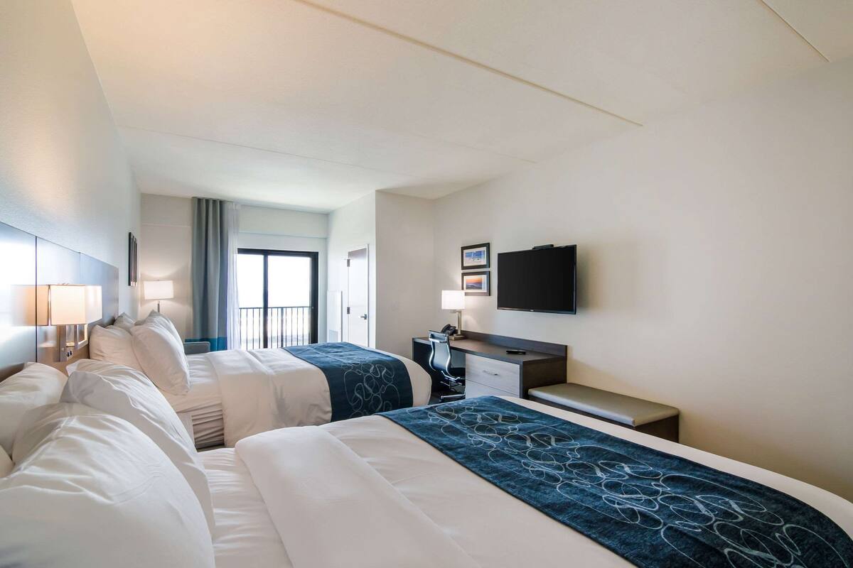 A hotel room with two beds, a desk, a TV, and a window with a view.