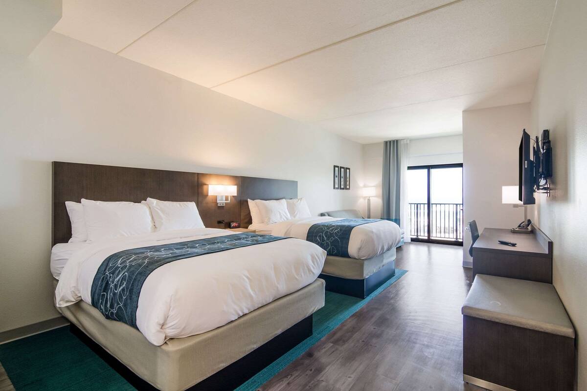 A hotel room with two beds, a desk, and a balcony.