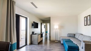 A modern hotel room with a sofa, a small table, a TV, a desk, and a floor lamp. - Comfort Inn & Suites Gulf Shores East Beach near Gulf State Park (Gulf Shores)