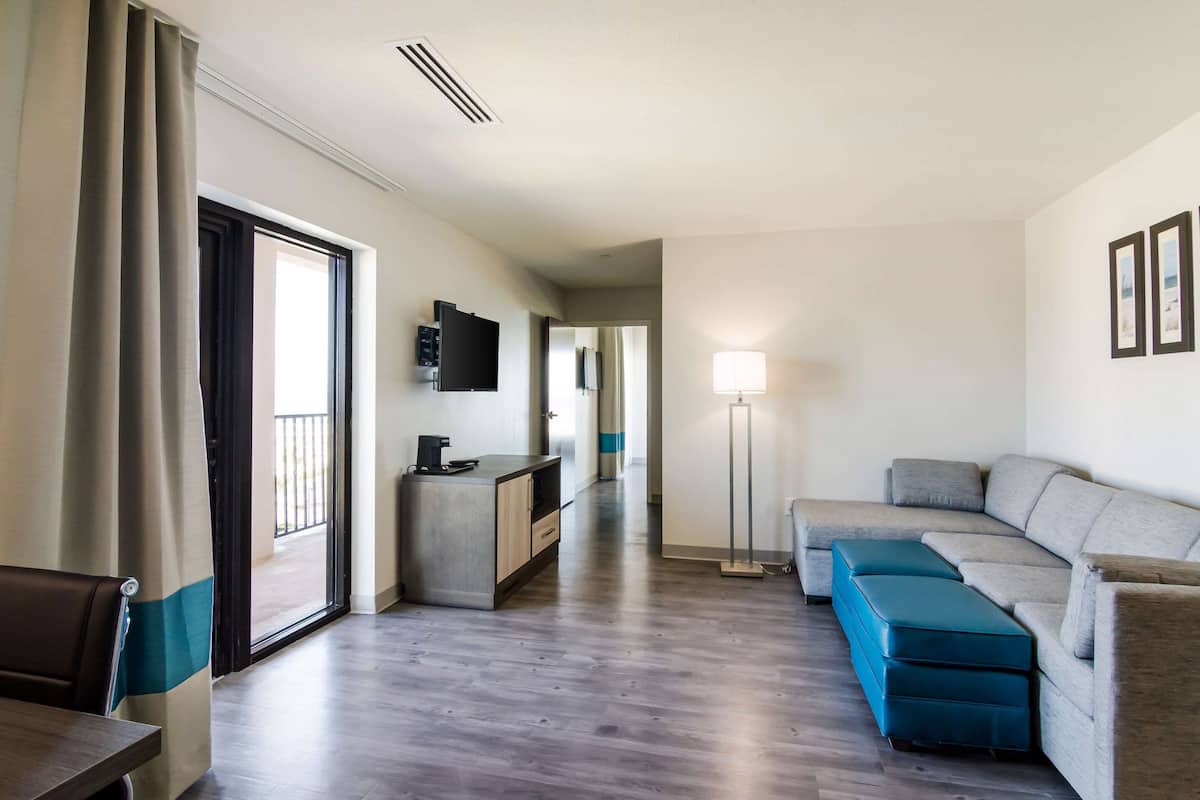 A modern hotel room with a sofa, a small table, a TV, a desk, and a floor lamp.