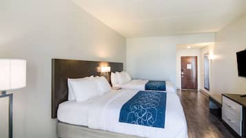 Habitación de hotel con dos camas, un escritorio, un televisor y un baño visible al fondo.