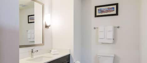 A bathroom with a white sink, a mirror, a toilet, and a framed picture on the wall.