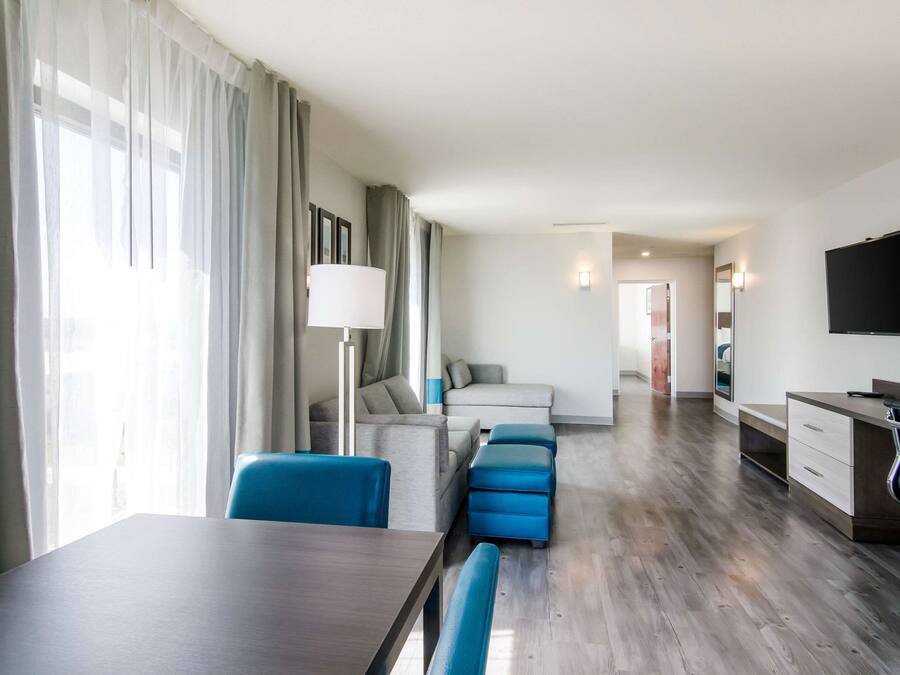 Una habitación de hotel moderna con zona de comedor, sofá, televisor y escritorio.