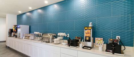 Een hotel receptie met een lange balie, koffieautomaten en een blauwe betegelde muur.