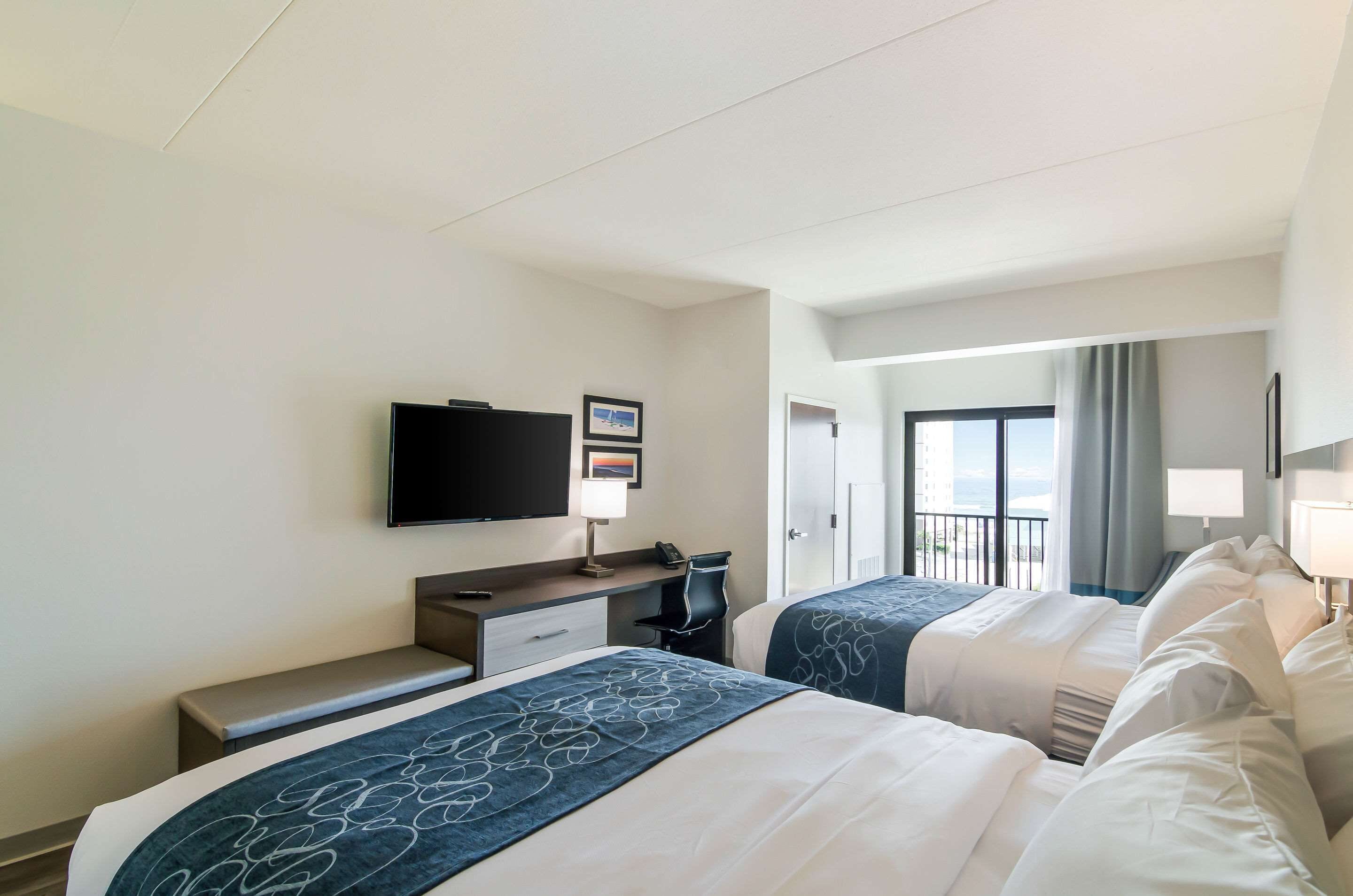 A hotel room with two beds, a desk, a chair, a television, and a balcony with a view.