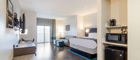 A hotel room with a bed, a desk, a chair, a microwave, and a refrigerator.