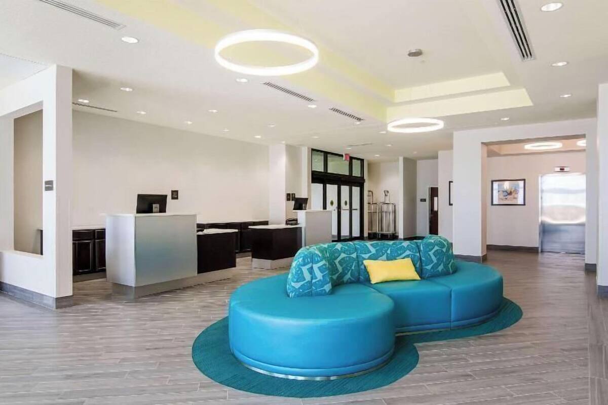 A modern lobby with a reception desk, a blue seating area, and a kitchen in the background.